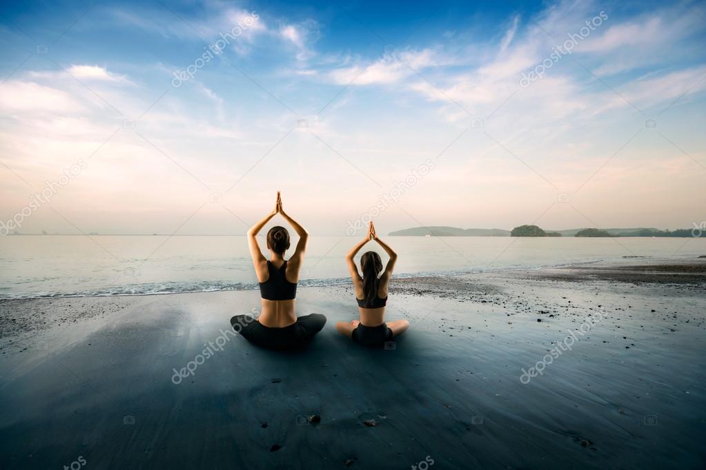 Mother and daughter doing yoga at beach