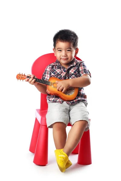 Pequeño chico asiático se sienta en una silla con una guitarra —  Fotos de Stock