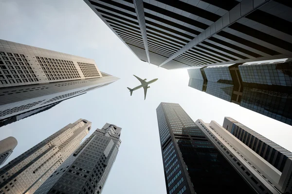 Edificios altos de la ciudad y un avión sobrevolando — Foto de Stock