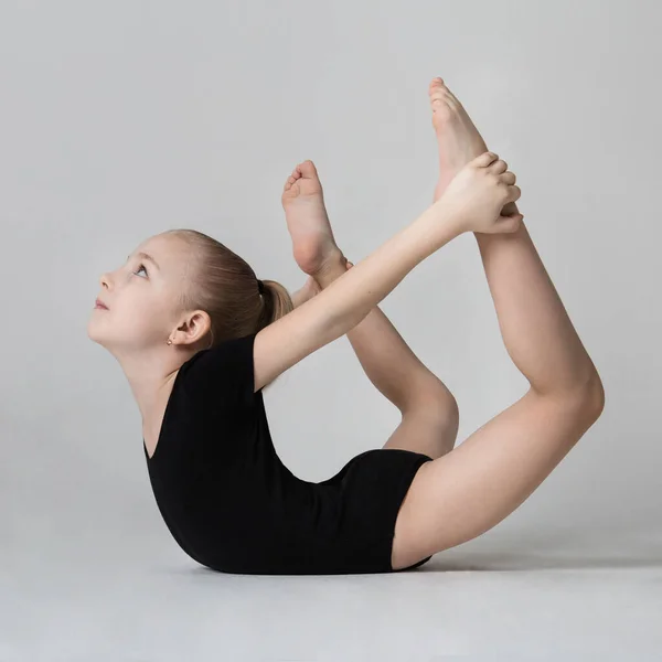 Una niña está de pie en una pose gimnástica, inclinándose sobre su estómago y sosteniendo sus piernas — Foto de Stock