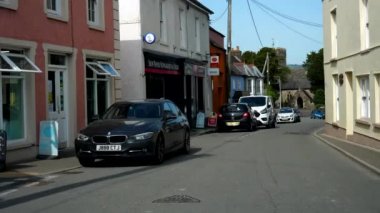 LLANGADOG, WALES, UNITED KINGDOM - CIRCA EPTEMBER, 2020: Galler köyü boyunca ana yolu kullanan ve canlı renkli evleri, postaneyi ve eski taş kilise binasını geçen araba öngörünümü.