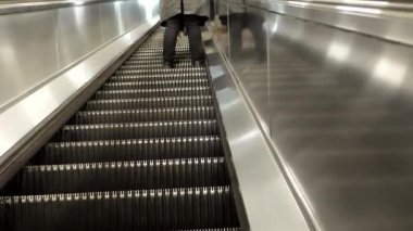 Uzun koyu gri bir ceket giymiş bir adamın merdivenleri ve bacakları görünüyor. Önünde yürüyen merdivenden yukarı çıkan bir adam daha var..