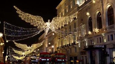 Londra, İngiltere, BİRLİK KINGDOM - CIRCA ARALIŞI 2020: Düşük açılı kırmızı ikonik otobüsler Noel sokak süslemeleri altında sürüş, Piccadilly Circus yakınlarında gece uçan melek.