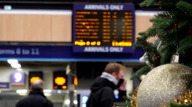 Koruyucu maskeler takan bulanık insanlar İngiltere 'nin Londra kentindeki Euston tren istasyonuna gelen ana kalkış panolarını izliyorlar..
