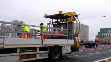 LONDON, UNITED KINGDOM - CIRCA NOVEMBER, 2020: Yüksek görüş açısına sahip yansıtıcı giysiler giyen yol işçileri, Vauxhall Köprüsü 'ndeki hareket halindeki kamyona trafik konilerini yüklüyorlar.