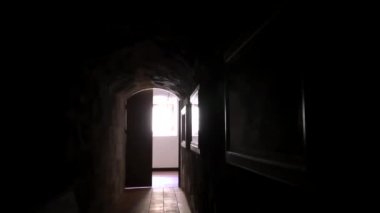 El kamerasının bakış açısı, Koyu kemerli tavan koridorunda yürüyen POV açık kapıdan parlak pencereye doğru metal parmaklıklarla ilerliyor.