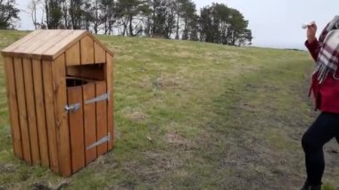 Kadın çöp tenekesine çöp atıyor. Güzel ahşap bir kutunun içinde. Yaya yolunun yanındaki tarlada çatısı olan bir kutu..