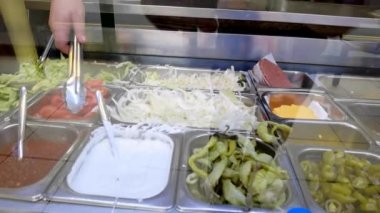 High Street 'in içinde ya da paket servis şefinde. Camın arkasındaki çeşitli sebzelerden yemek maşasıyla çeşitli sebzeler topluyor. El kamerasını kapat..