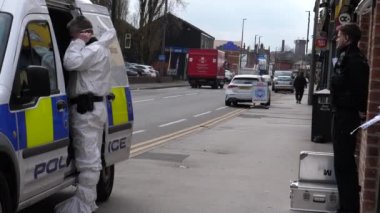 MANCHESTER, BİRLİK KINGDOM - 13 Nisan 2021: Olay yeri inceleme ekibi, polis aracının yanında işe hazırlanırken siyah üniformalı polis memuru kanıt konteynırını ve kapıyı koruyor..