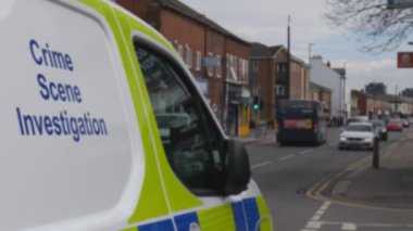 Salford, İngiltere 'de polis olay yeri inceleme minibüsünün önünden geçerken dikkati dağılmış sokak trafiği görülüyor..