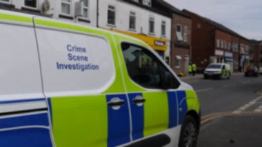 Salford, Greater Manchester, İngiltere 'nin kuzeybatısındaki suç mahallinin yakınındaki iki polis minibüsü ve memurun görüntüsü bulanık..