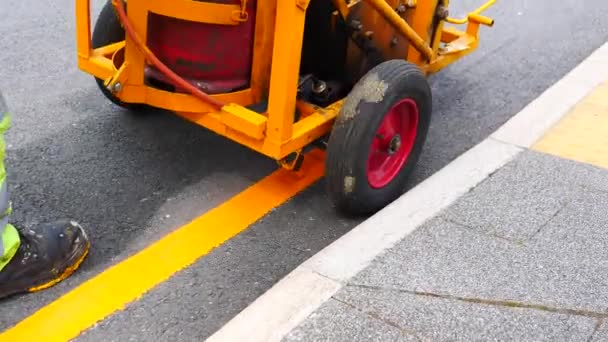 明るい安全制服の手動労働者は 道路アスファルト曲げ ハンドヘルドカメラショットに加熱塗料と道路マーキングマシン塗装黄色のラインを押している — ストック動画