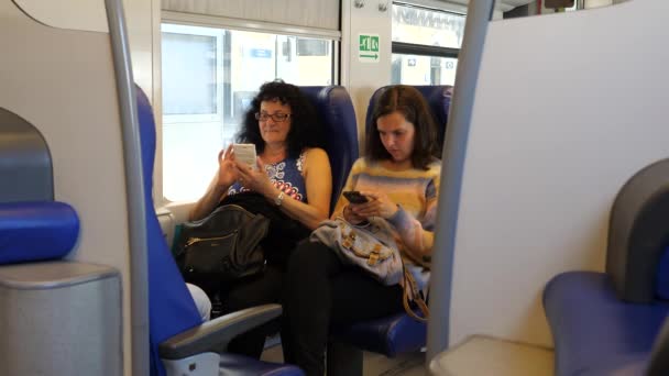 静電車の中に座って携帯電話をサーフィンしている若い大人と50代の女性が — ストック動画