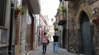 Sicilya 'nın dar sokaklarında yürüyen üç turistin ailesi ya da grubu. Randazzo, evin duvarında asılı çiçeklerin fotoğrafını çeken kadın..