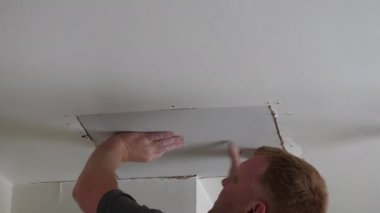 Man, plasterer covering hole in the domestic room ceiling with piece of plasterboard after water leak repair.