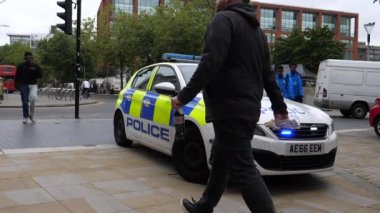 MANCHESTER, İngiltere, BİRLİK KINGDOM - CIRCA EPTEMBER, 2021: Birçok insan Piccadilly Gardens 'ın kaldırımlarında ya da yaya bölgesinde parlayan mavi acil durum ışıklarıyla polis arabasının yanından geçiyor.