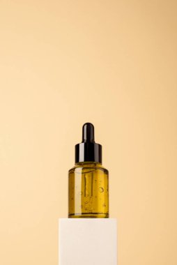 Biege arka planında beyaz podyumda siyah kapaklı yeşil cam damlatıcı şişesi..