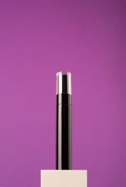 Beyaz podyum ve mor arka planda şeffaf kapaklı siyah maskara tüp..