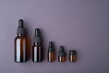 Kehribar cam damlaları gri arka planda farklı boyutlarda şişeler.