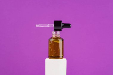 Mor arka planda beyaz podyumda pipeti olan yeşil cam damlatıcıyı aç