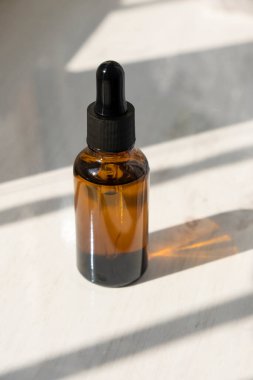 Siyah kapaklı kehribar cam damlası şişesi ve camdan gelen güneş ışığı..