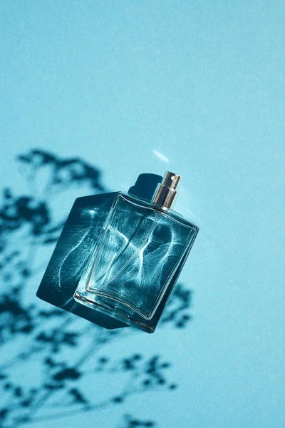 Frasco transparente de perfume sobre fondo azul. Presentación de fragancias con luz natural — Foto de Stock