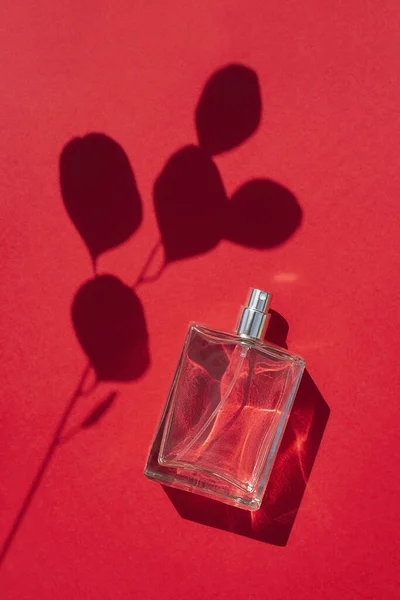 Transparent bottle of perfume on a red background. Fragrance presentation with daylight. — Stock Photo, Image