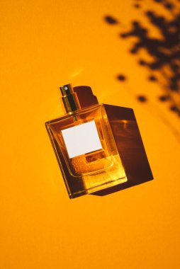 Turuncu arka planda saydam bir parfüm şişesi. Gün ışığıyla parfüm sunumu