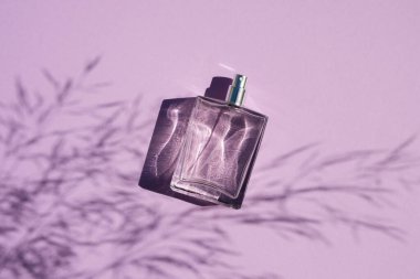 Leylak arka planında şeffaf bir parfüm şişesi. Gün ışığıyla parfüm sunumu.