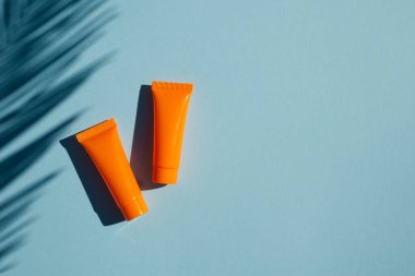 Krema ya da palmiye yapraklı losyon için iki plastik turuncu şişe. Mavi arkaplandaki üst görünüm. Cilt kremi kozmetik. Yüz bakımı için güzellik konsepti