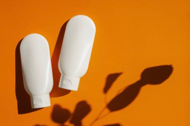 Turuncu arka planda krem ya da losyon için iki plastik beyaz tüp. Cilt kremi kozmetik.