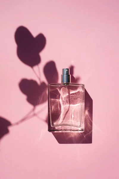 Прозрачная бутылка духов на розовом фоне. Презентация аромата с дневным светом — стоковое фото