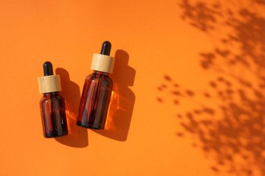 Kehribar cam damlaları farklı boyutlarda, turuncu arka planda bambu kapaklı. Bitki gölgesi olan üst görünüm.