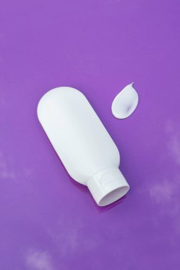 Krem veya losyon için plastik beyaz tüp ve mor arka planda kremin dokusunun görünümü .