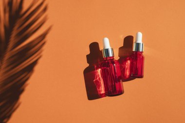 Turuncu arka planda gümüş kapaklı kırmızı cam damlalar. Güzel gün ışığında cilt bakımı ürünleri.