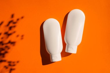 Turuncu arka planda krem ya da losyon için iki plastik beyaz tüp. Cilt kremi kozmetik.