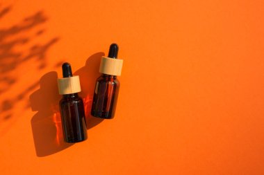 Kehribar cam damlaları farklı boyutlarda, turuncu arka planda bambu kapaklı. Bitki gölgesi olan üst görünüm.