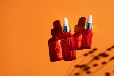 Turuncu arka planda gümüş kapaklı kırmızı cam damlalar. Güzel gün ışığında cilt bakımı ürünleri.
