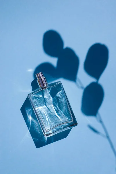 Transparente Flasche Parfüm auf blauem Hintergrund. Duftpräsentation mit Tageslicht. — Stockfoto