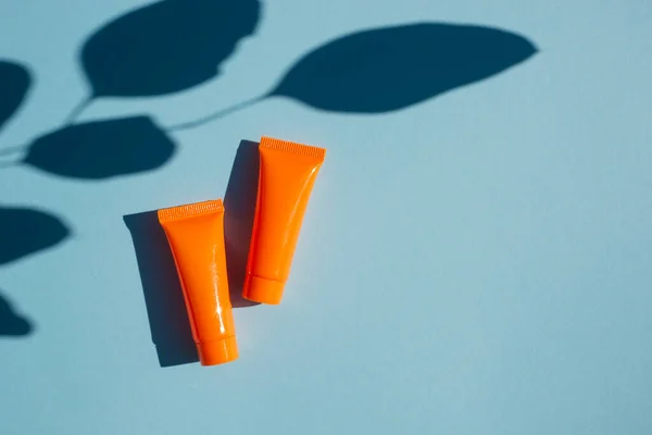 두 개 의 플라스틱 오렌지 병에 크림 이나 종려나무 잎이 달린 로션 이 그늘을 드리운다. 푸른 배경 위의 맨 위 사진. — 스톡 사진