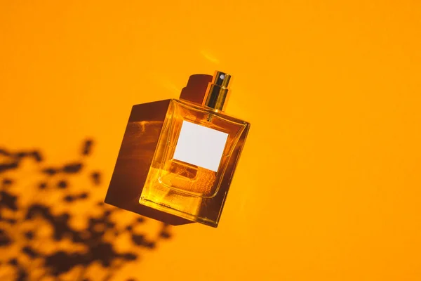 Frasco transparente de perfume sobre fondo naranja. Presentación de fragancias con luz natural — Foto de Stock