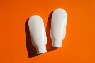 Turuncu arka planda krem ya da losyon için iki plastik beyaz tüp..