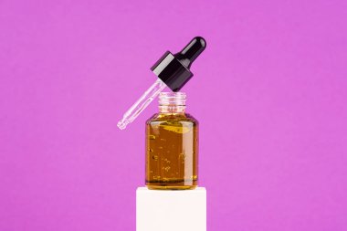 Mor arka planda beyaz podyumda pipeti olan yeşil cam damlatıcıyı aç