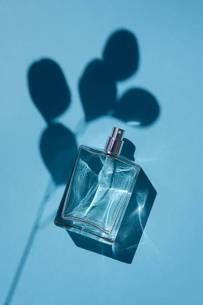 Transparente Flasche Parfüm auf blauem Hintergrund. Duftpräsentation mit Tageslicht. — Stockfoto