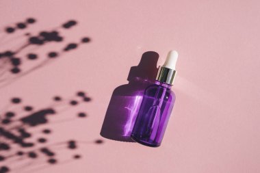 Metalik kapaklı mor cam damlacık şişesi. Bitki gölgesi ile gül arkaplanının üst görünümü.