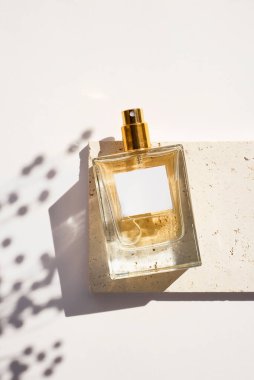 Beyaz arka planda beyaz etiketli saydam bir parfüm şişesi. Gün ışığıyla güzel kokulu bir sunum. Kuru bitki ile doğal maddelerin moda konsepti. Kadın ve erkeğin özü..