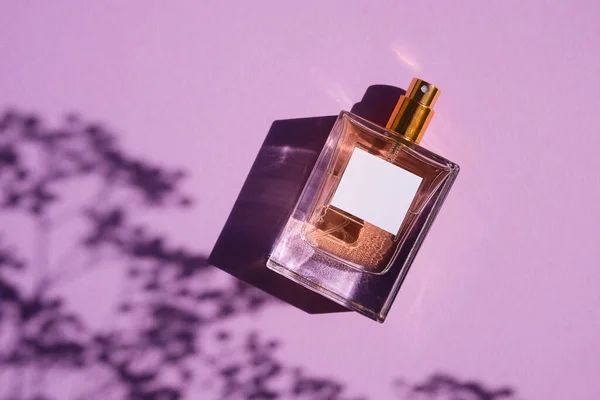 Transparente Flasche Parfüm auf fliederfarbenem Hintergrund. Duftpräsentation mit Tageslicht. — Stockfoto