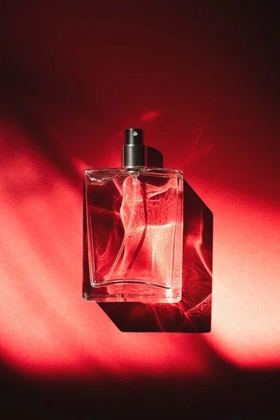 Διαφανές μπουκάλι άρωμα σε κόκκινο φόντο. Παρουσίαση αρώματος με φως ημέρας. — Φωτογραφία Αρχείου