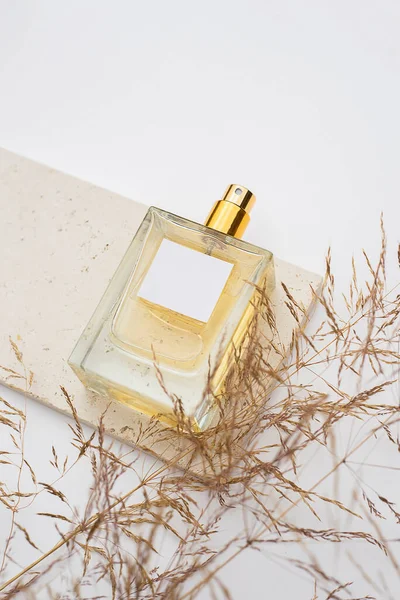 Frasco transparente de perfume sobre plato de piedra sobre fondo blanco. Presentación de fragancias con luz natural. — Foto de Stock