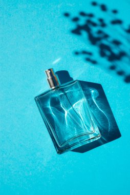 Mavi arka planda saydam bir parfüm şişesi. Gün ışığıyla parfüm sunumu